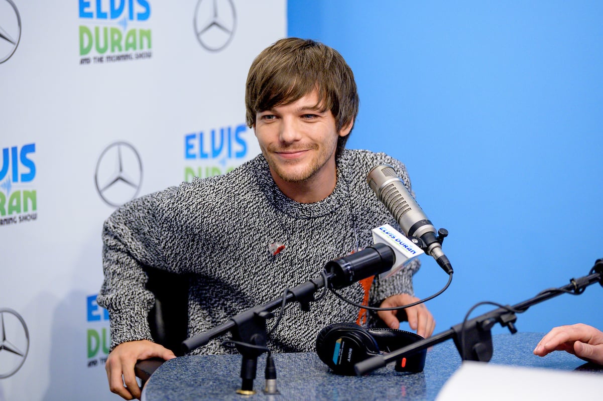 Louis Tomlinson from One Direction smiles in a grey sweater at the Elvis Duran show
