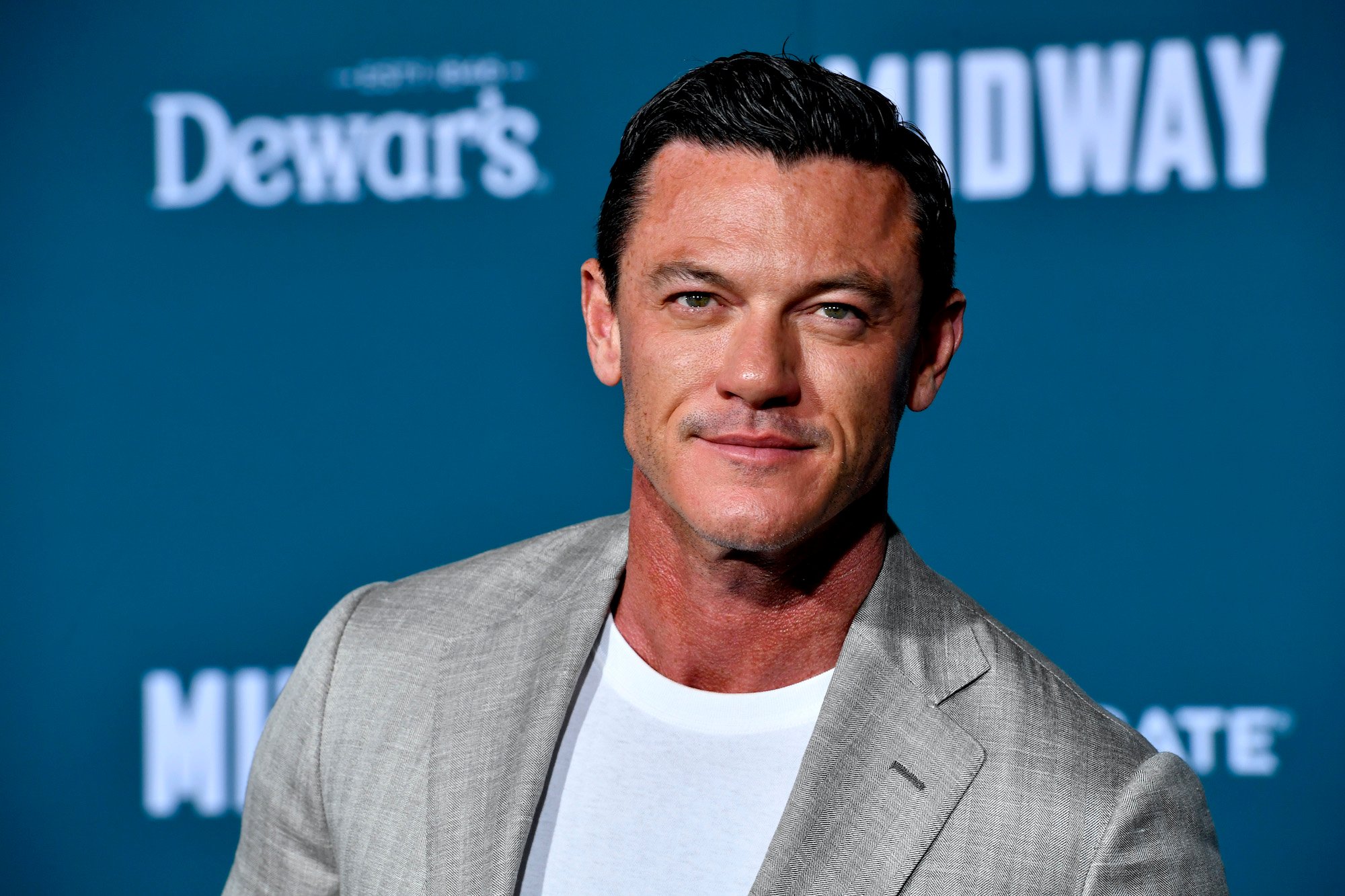 Luke Evans smiling in front of a blue background