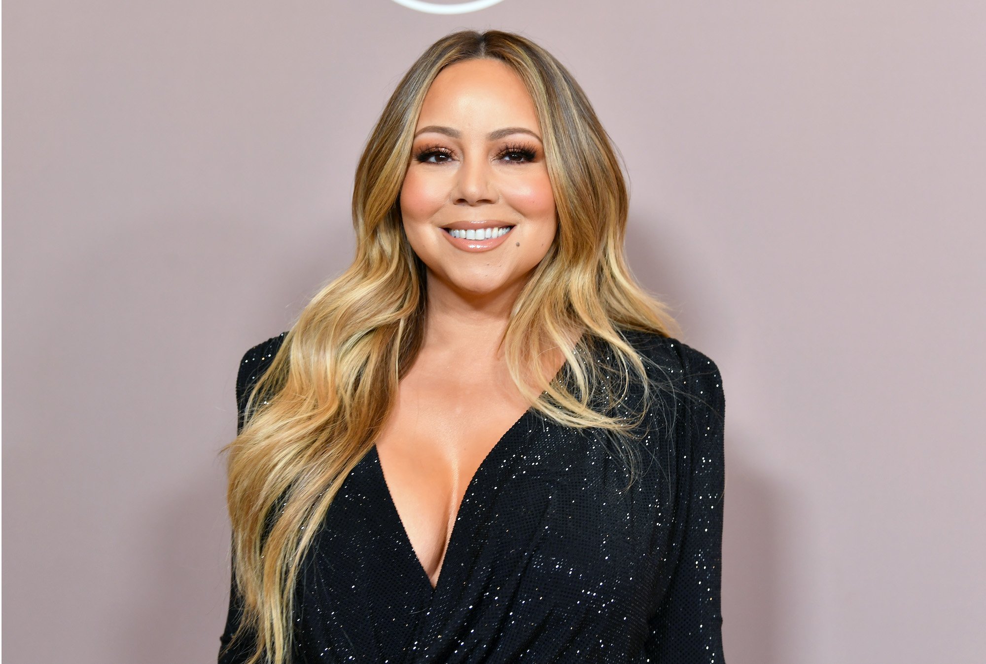 Mariah Carey smiling in front of a pink background