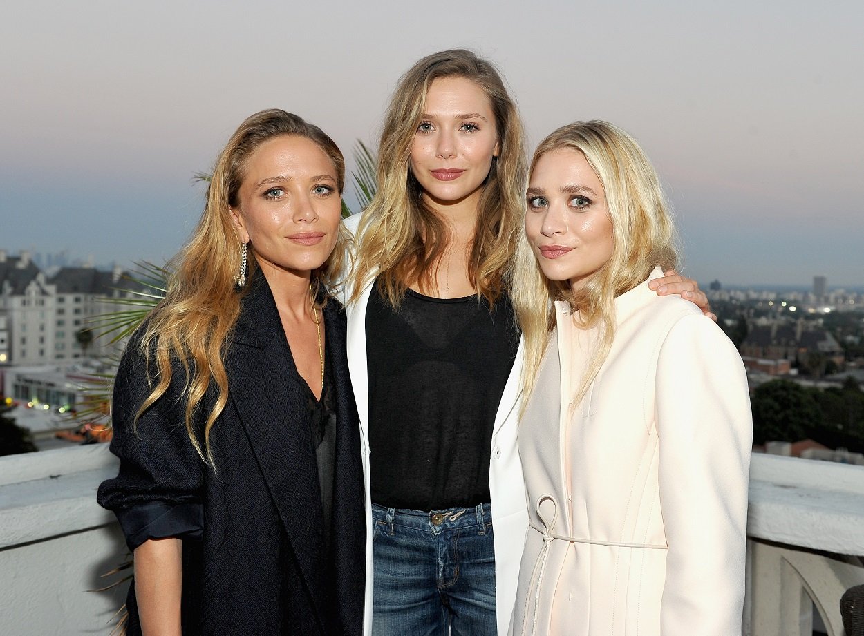 Sisters Mary-Kate Olsen, Elizabeth Olsen, and Ashley Olsen smile softly at the camera