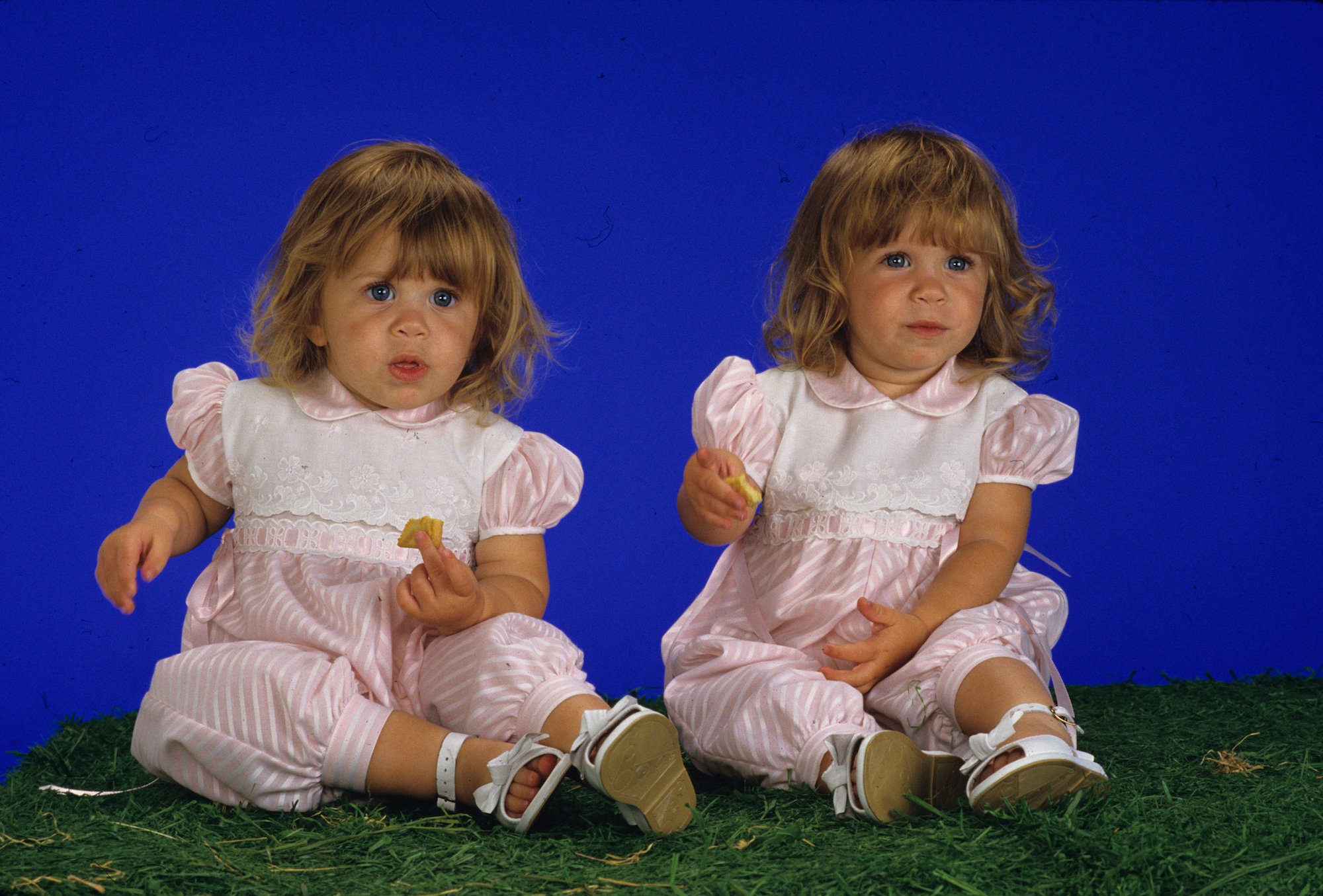 Ashley and Mary-Kate Olsen as babies, sitting in front of a blue background