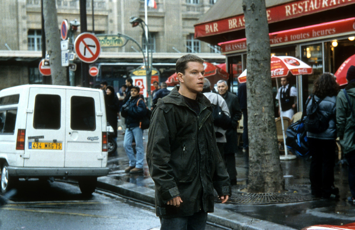 Matt Damon stands in the street while people stand on the sidewalk during the filming of 'The Bourne Identity'