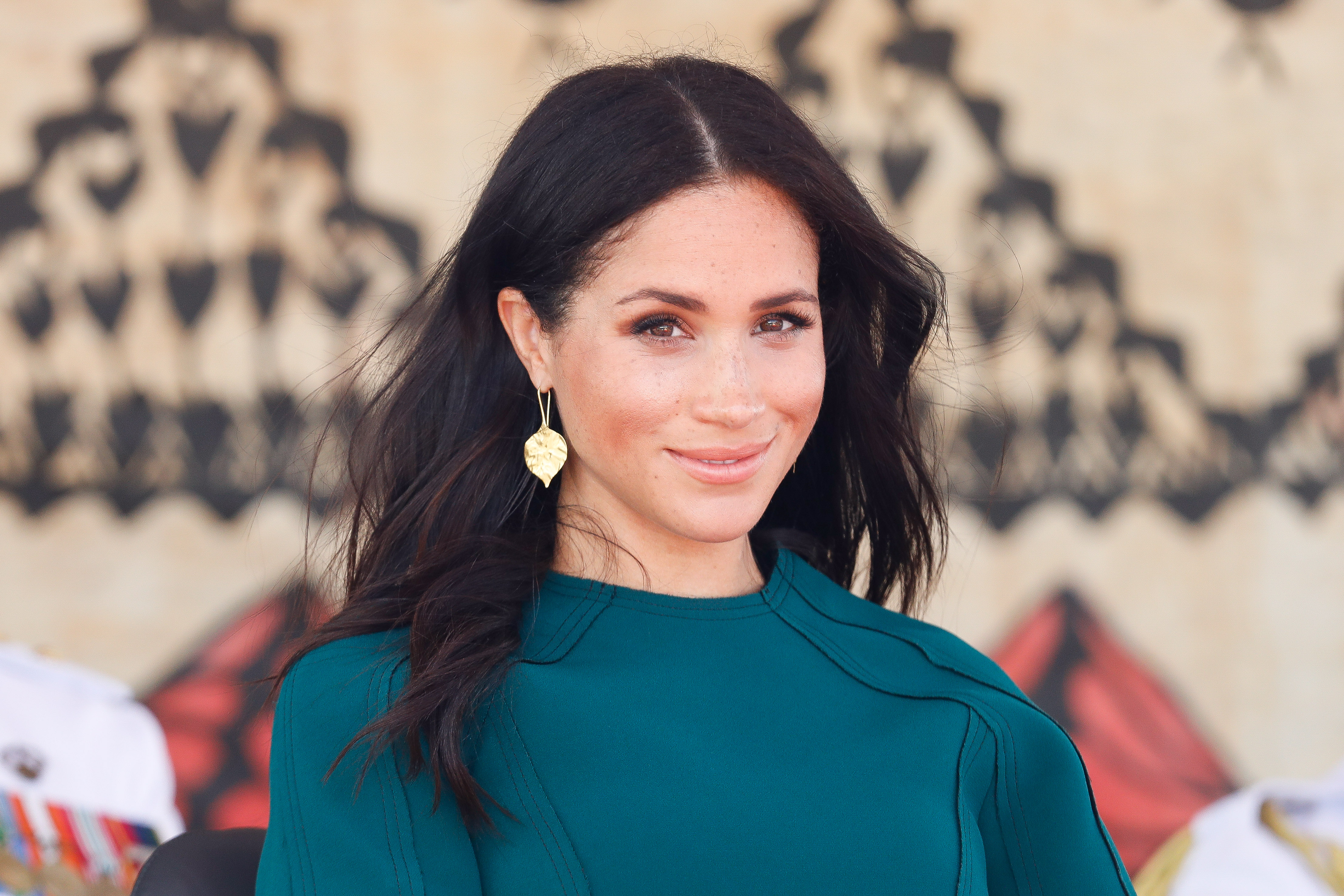 Meghan Markle sitting down and smiling in a turquoise outfit at the unveiling of the Labalaba Statue in Fiji