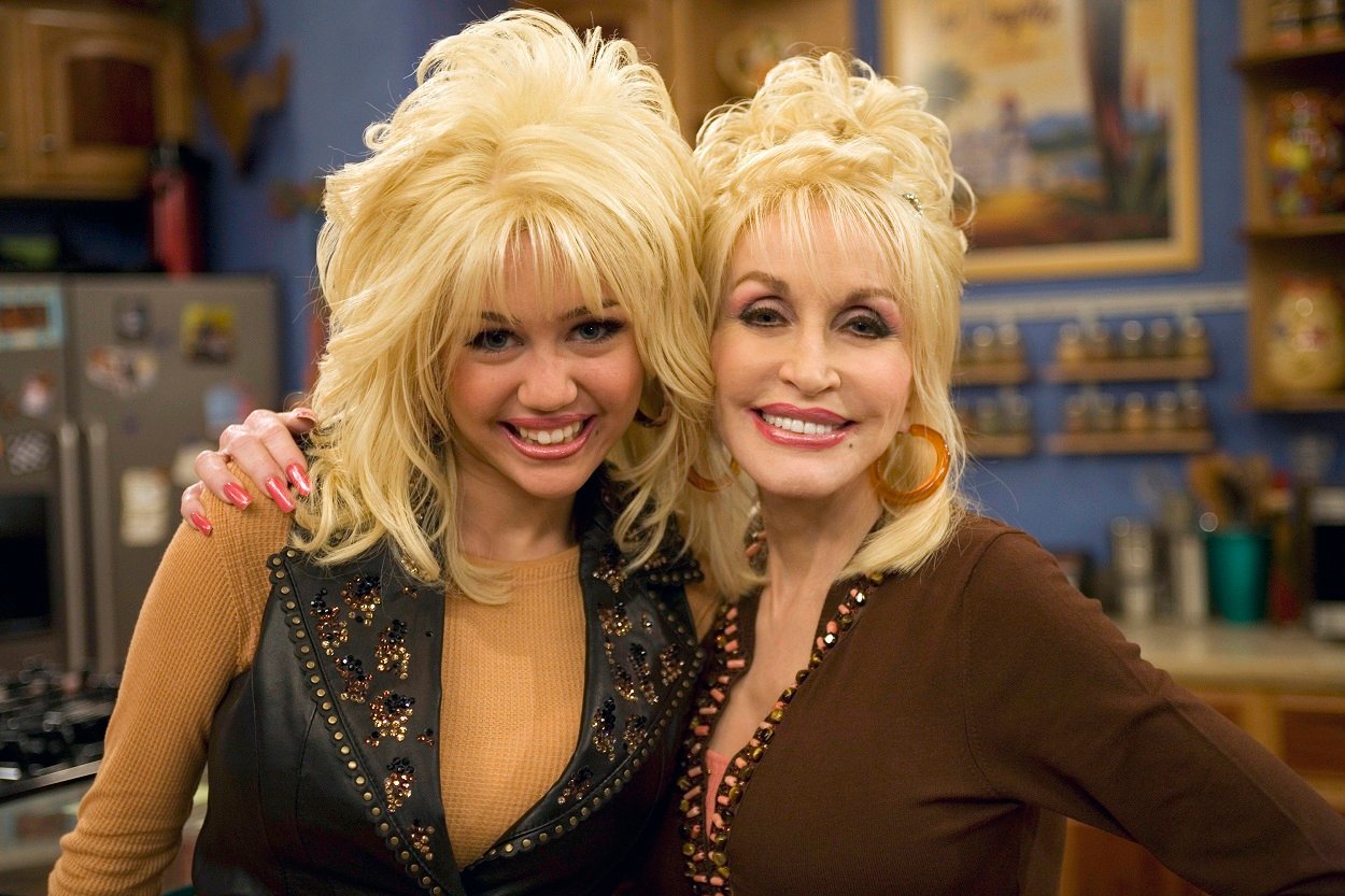 Miley Cyrus as Hannah Montana and Dolly Parton smile at the camera in bedazzled tops and blonde wigs
