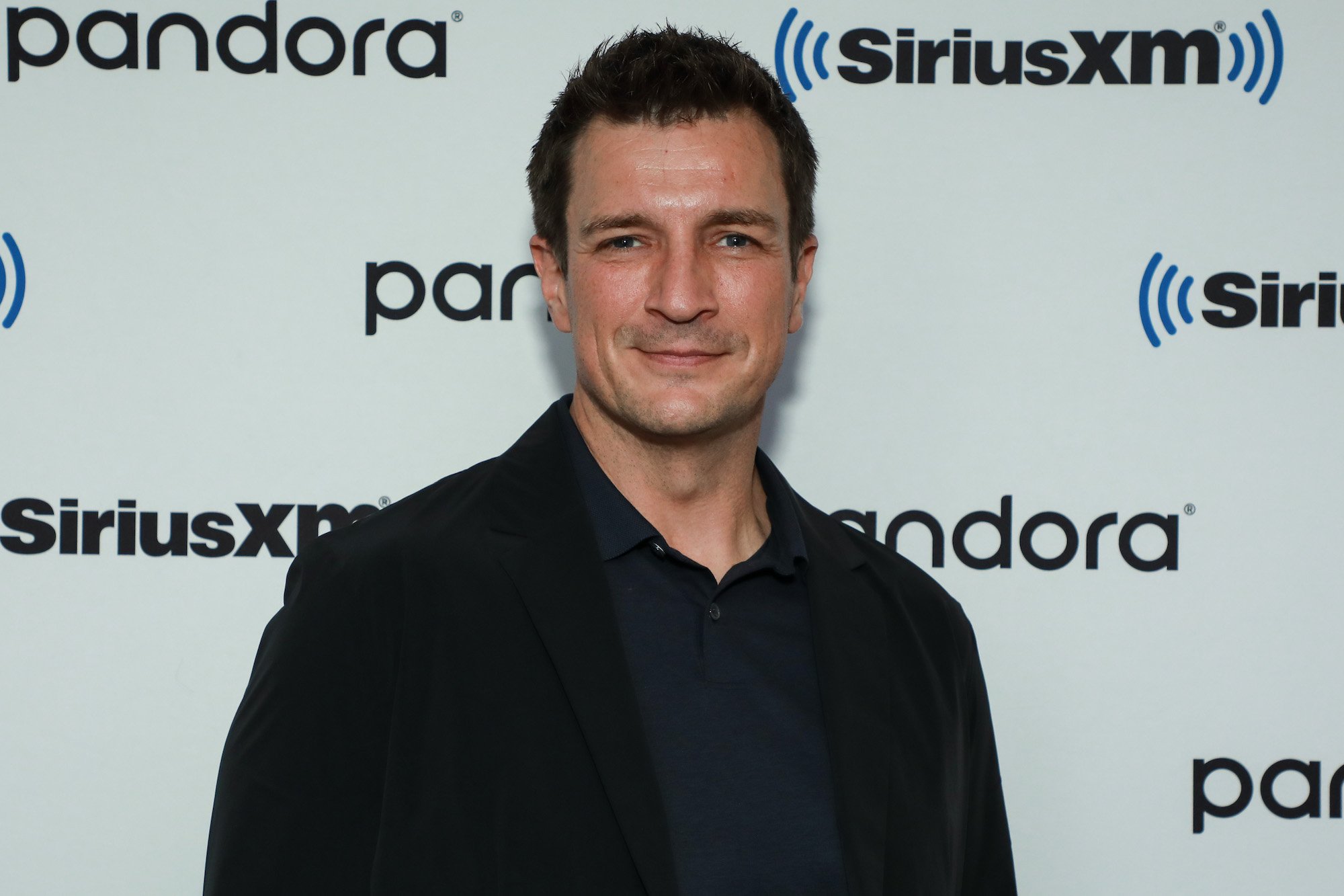 Nathan Fillion smiling in front of a white background
