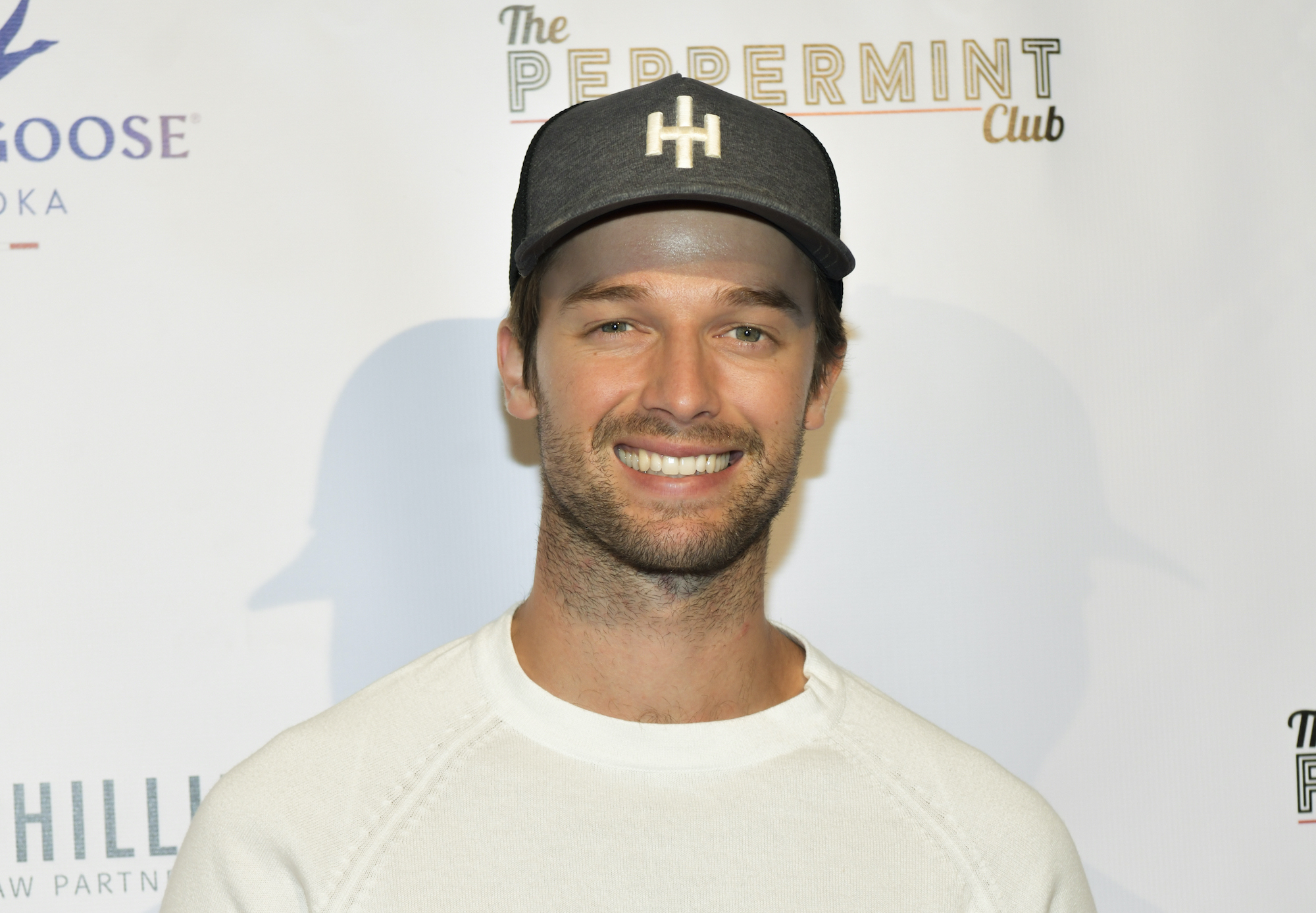 Patrick Schwarzenegger smiling in front of a white background