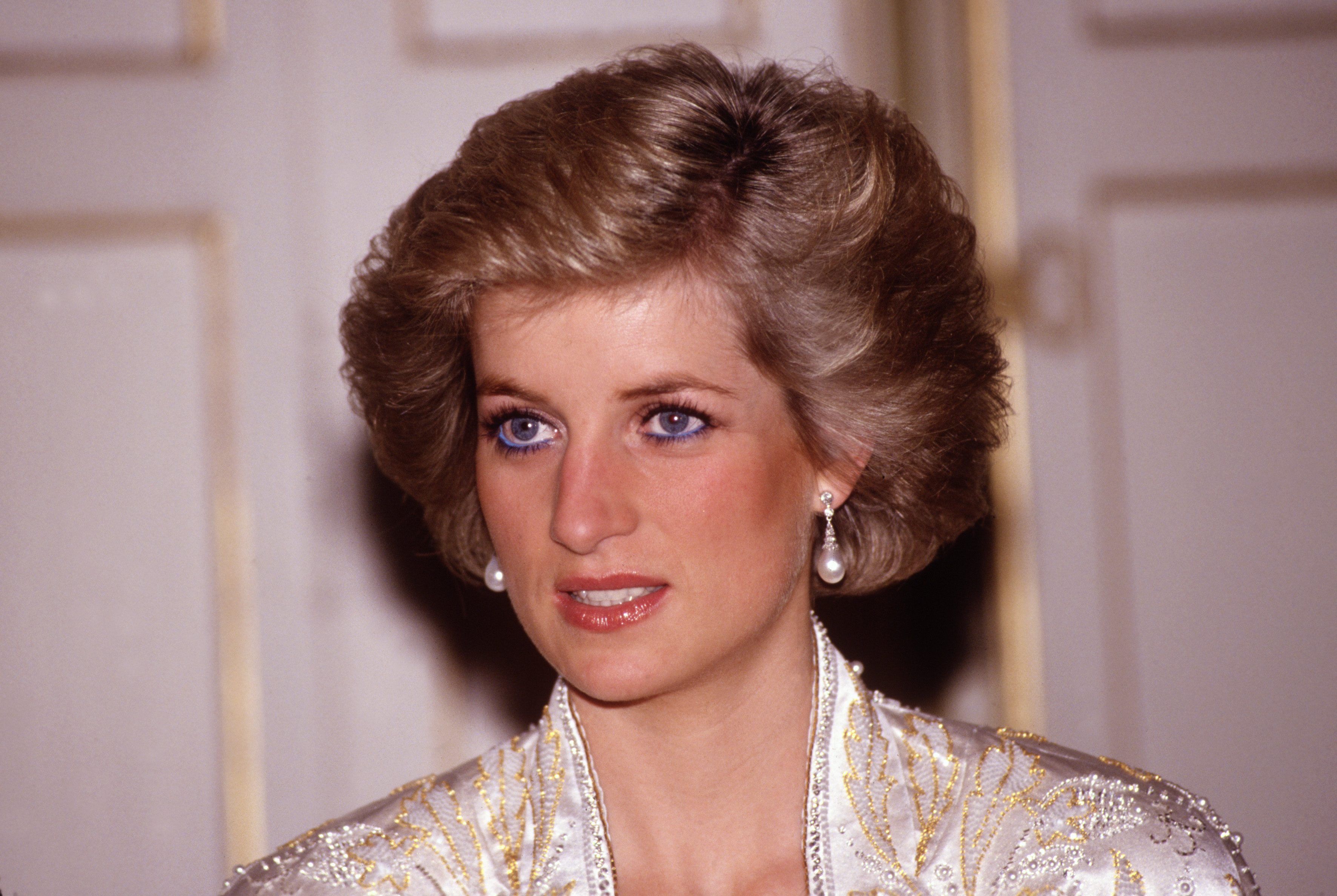 Photo of Princess Diana from the shoulders up wearing pearl-drop earrings and her signature blue eyeliner