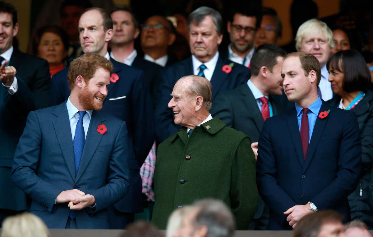 Prince Harry and Prince Philip smiling at each other as Prince William looks on.