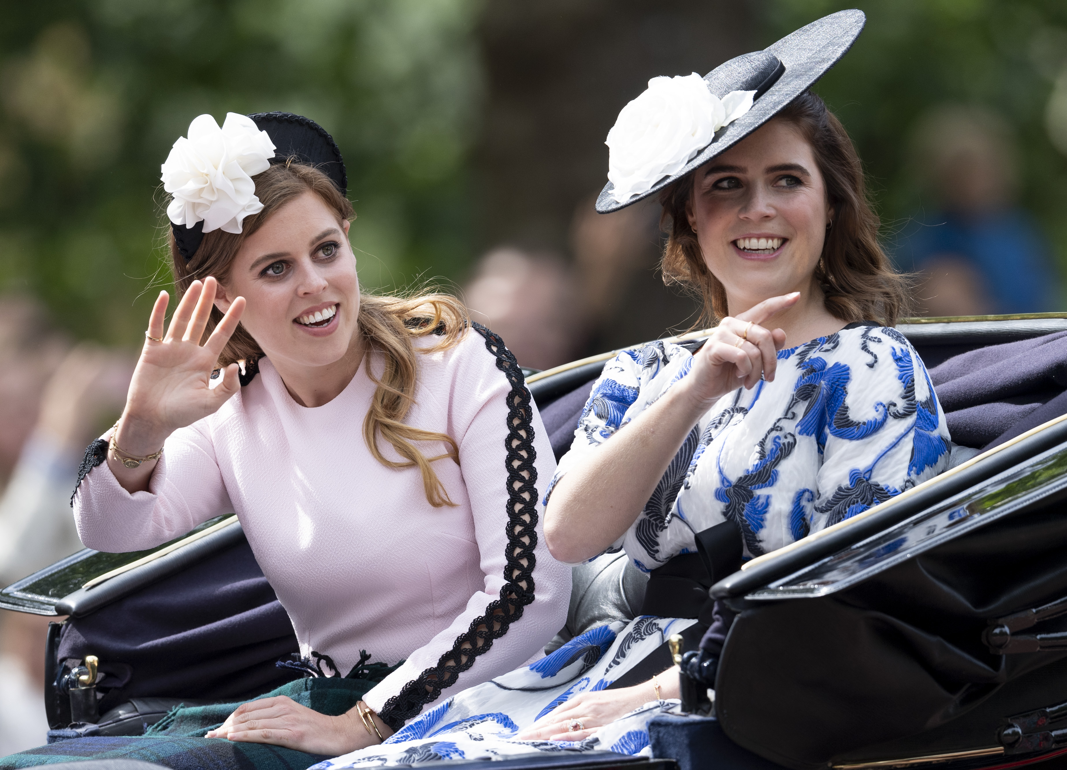 Princess Beatrice and Princess Eugenie riding in a carriage smiling and pointing to crowd during Trooping The Colour