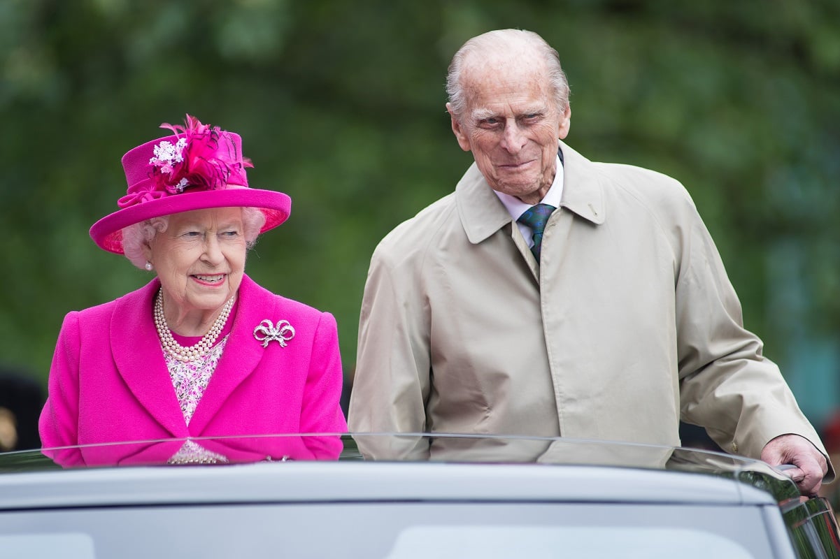 Queen Elizabeth II dressed in a bright pink outfit and hat next to Prince Philip smiling in a light-colored coat