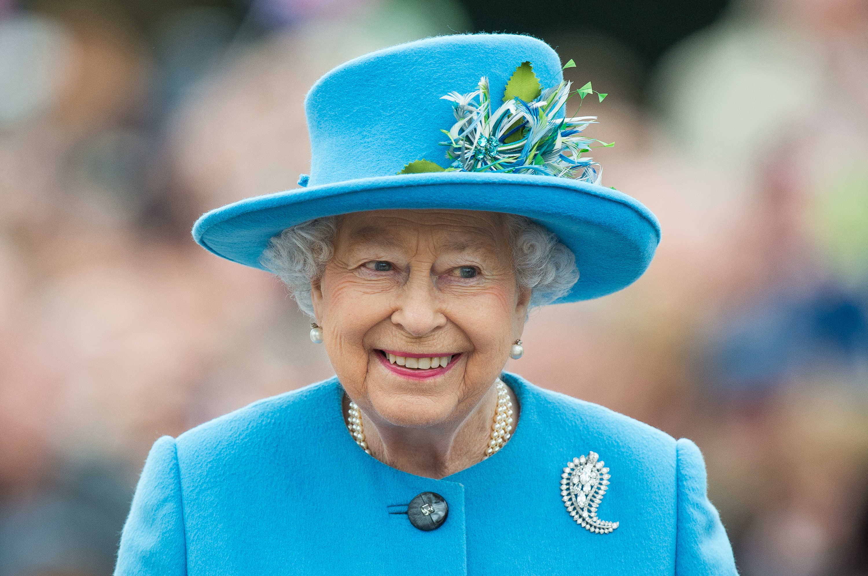 Queen Elizabeth II smiling during tour of Queen Mother's Square dressed in a baby blue hat and matching blazer
