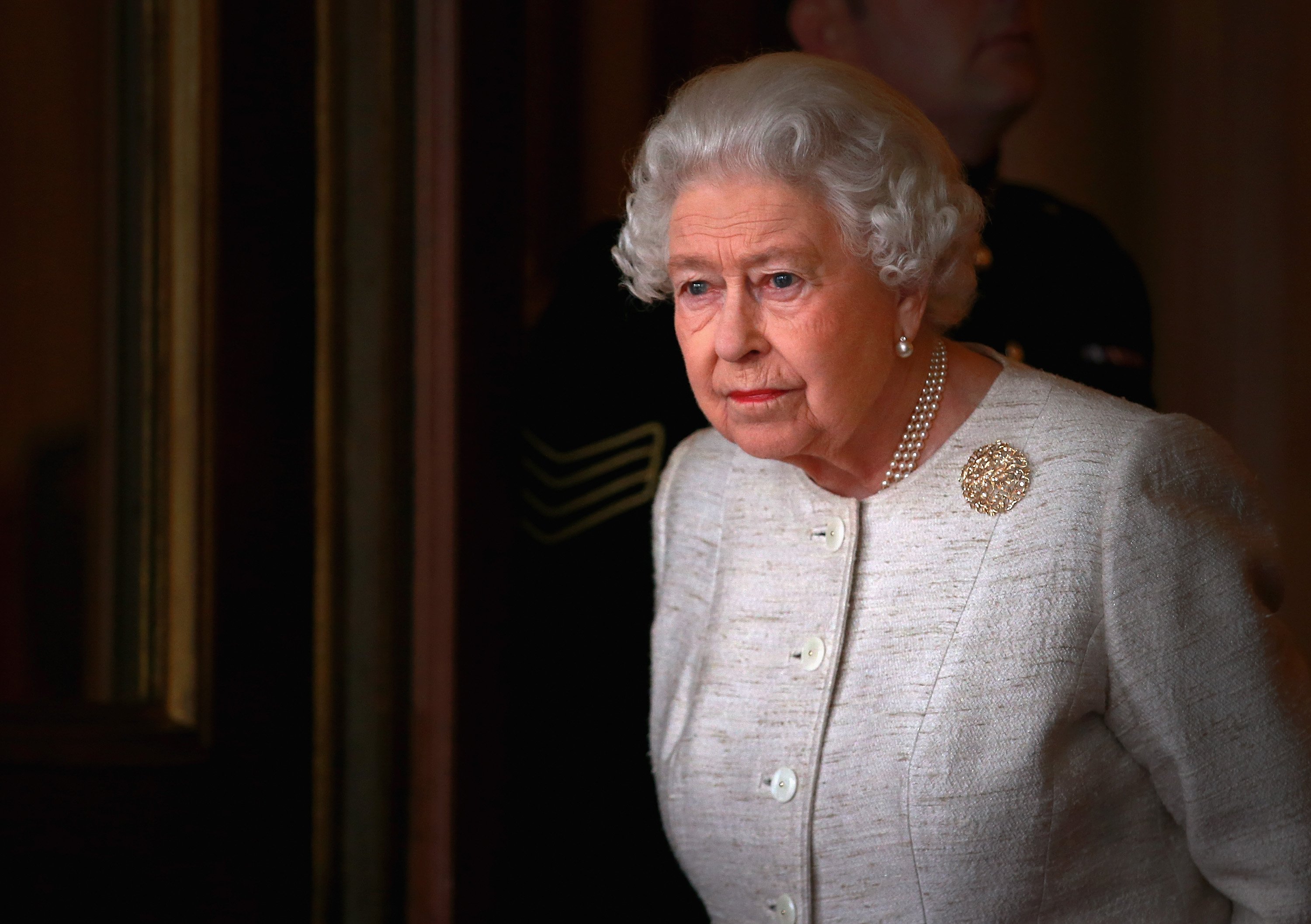 Queen Elizabeth II standing in Buckingham Palace looking somber