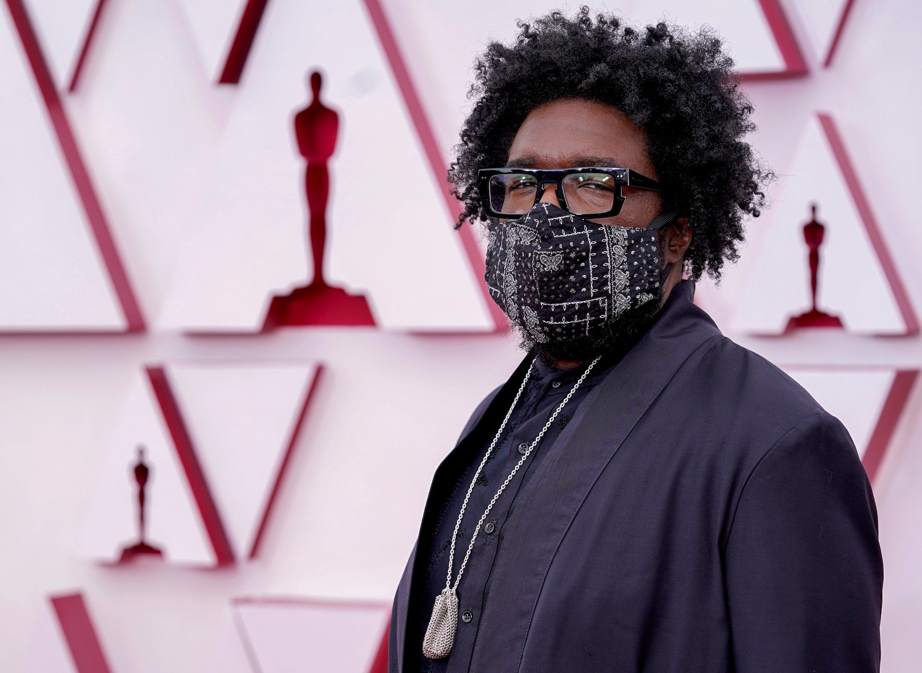 Questlove, one of the best dressed at the Oscars in 2021, wearing a mask and a black suit with a gold chain on the red carpet