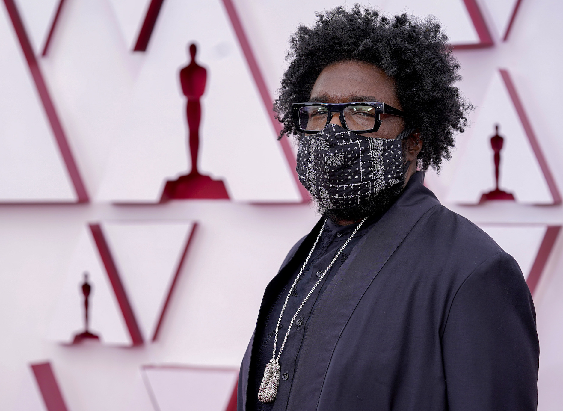 Questlove, one of the best dressed at the Oscars in 2021, wearing a mask and a black suit with a gold chain on the red carpet