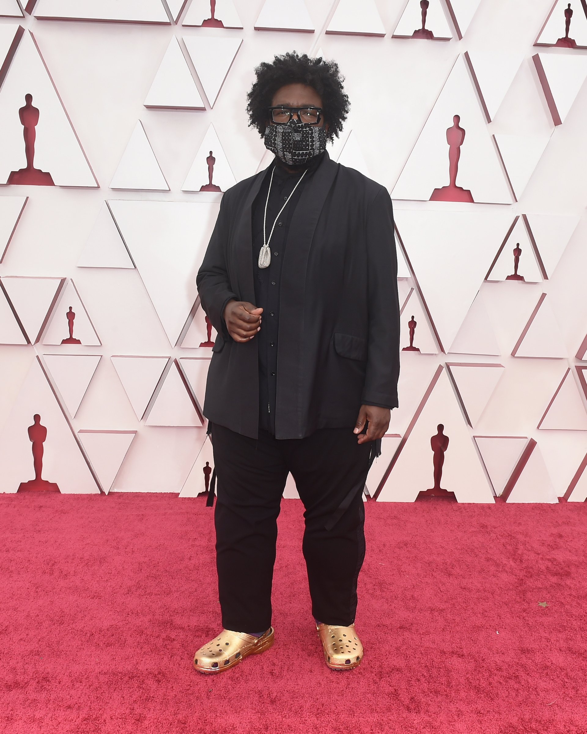 Questlove's Oscars look on the red carpet complete with a mask, a suit, and gold crocs