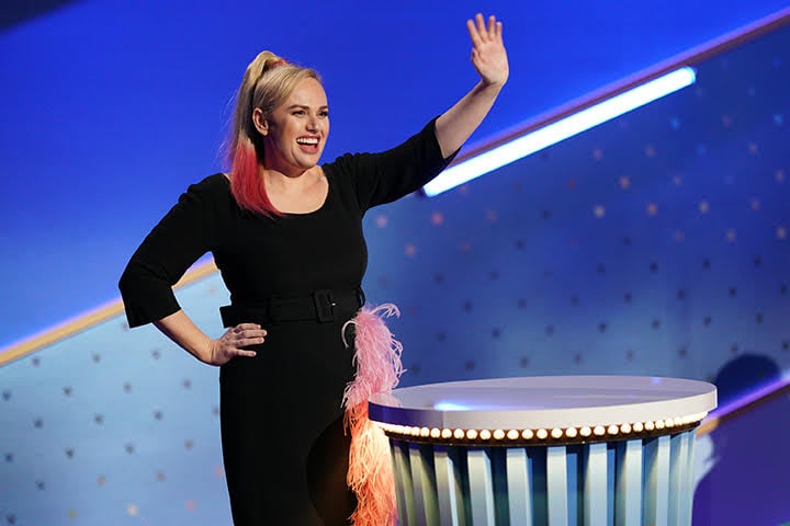 Rebel Wilson stars as host of 'Pooch Perfect', coming on stage waving in a black dressa