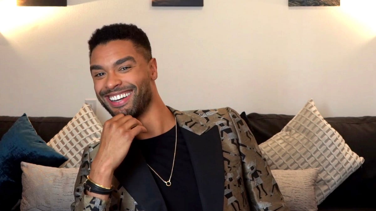 Regé-Jean Page smiles into the camera for a seated position on the couch