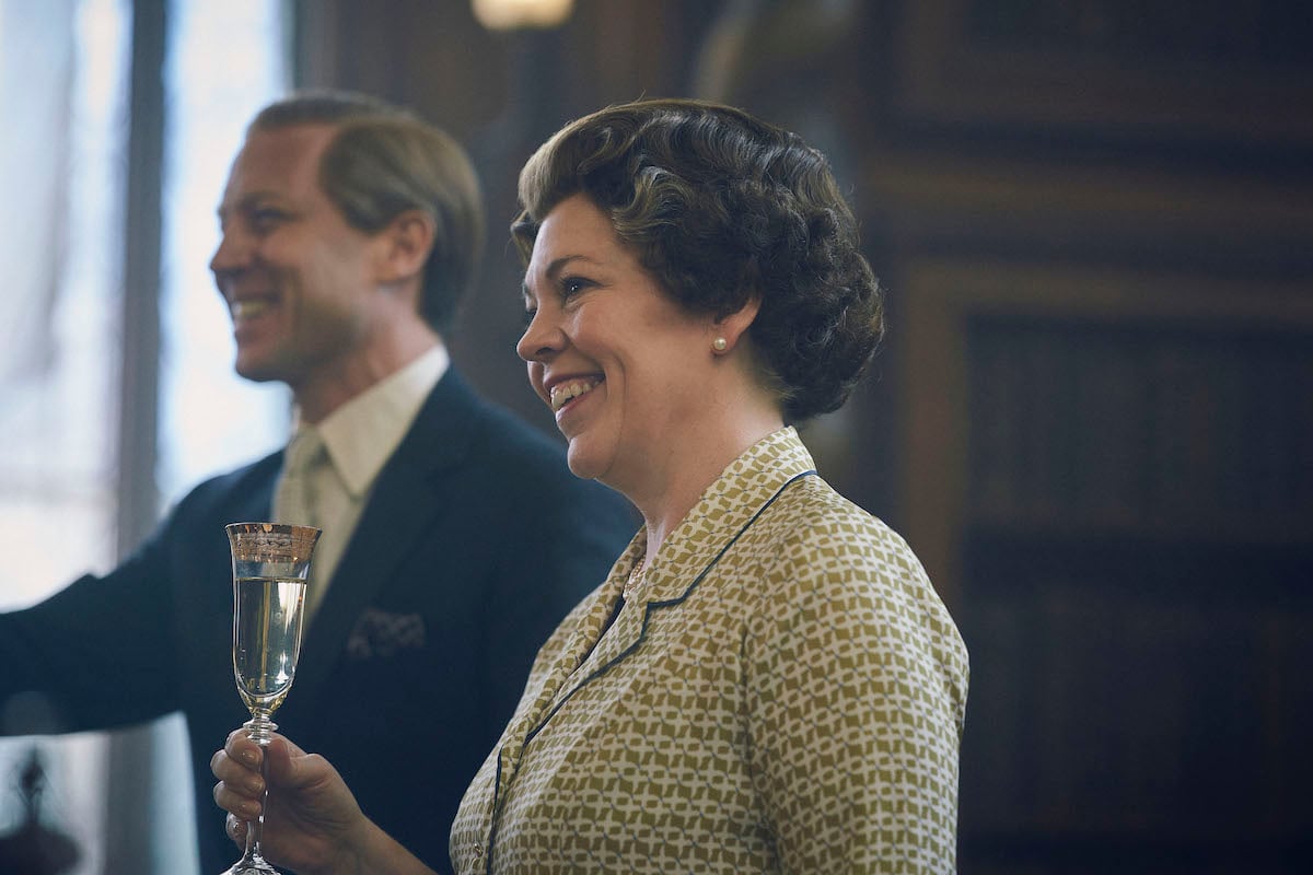 Prince Philip and Queen Elizabeth II are standing up with their glasses raised in 'The Crown'