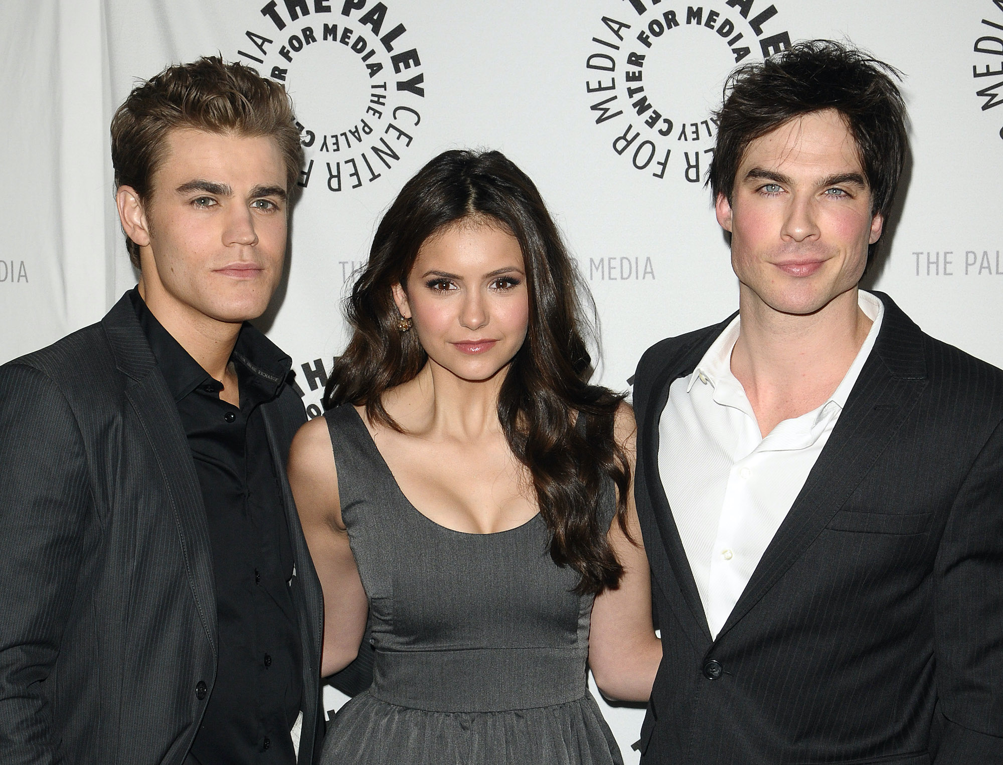 (L-R) Paul Wesley, Nina Dobrev, and Ian Somerhalder smiling in front of a white background