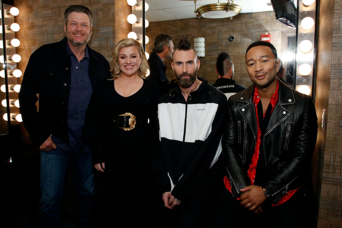 Blake Shelton, Kelly Clarkson, Adam Levine, and John Legend stand in front of a lit mirror at the 2019 NBCUniversal Upfront