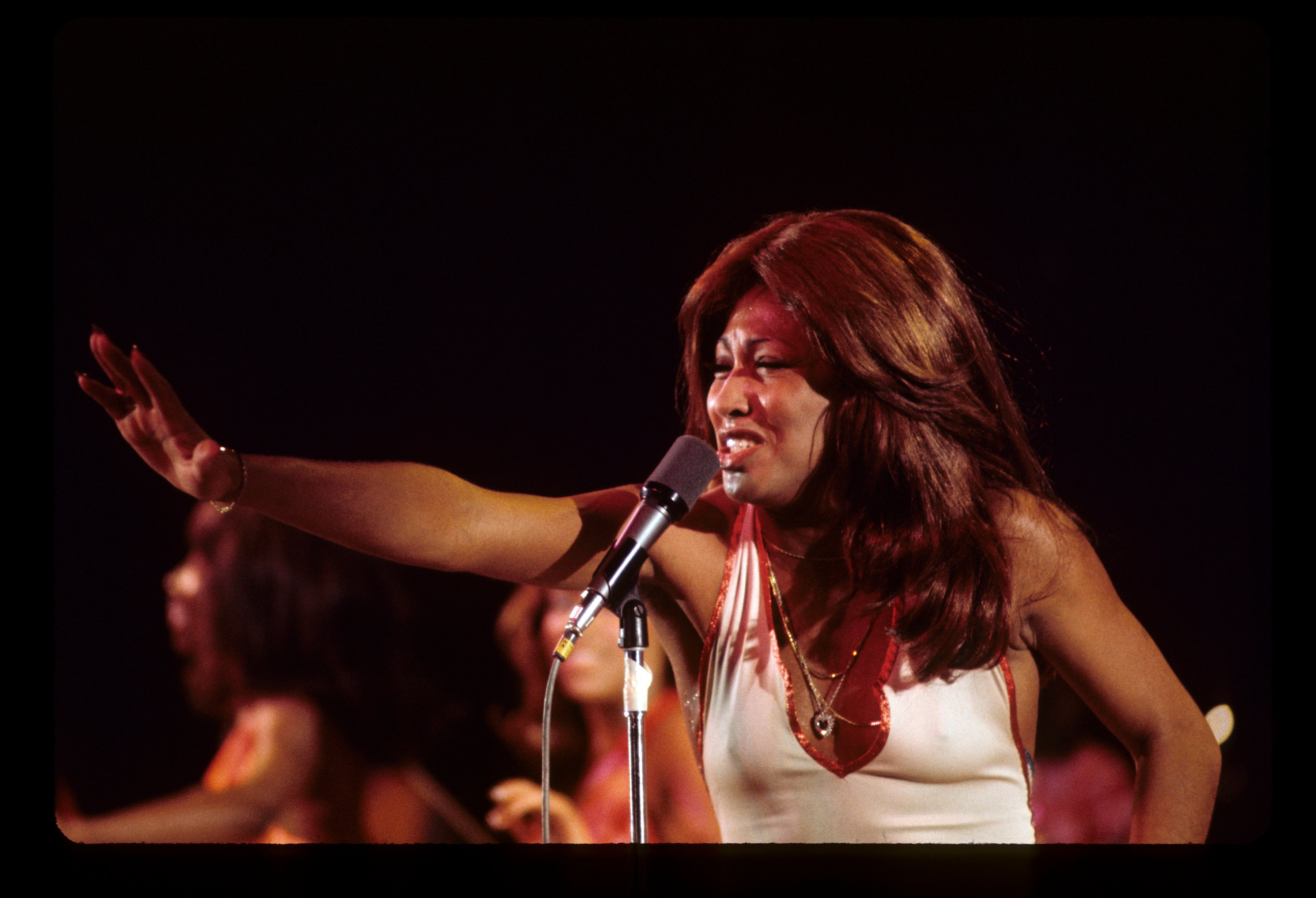 Tina Turner extends her hand while singing on stage