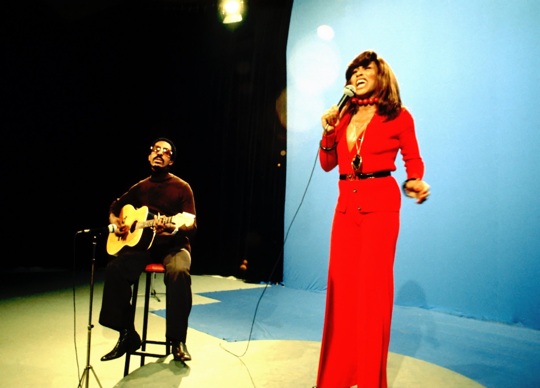 Tina Turner sings in a red dress while Ike Turner sits and plays guitar