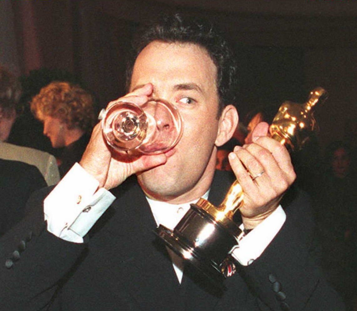 Tom hanks drinking a dink while holding his Oscar