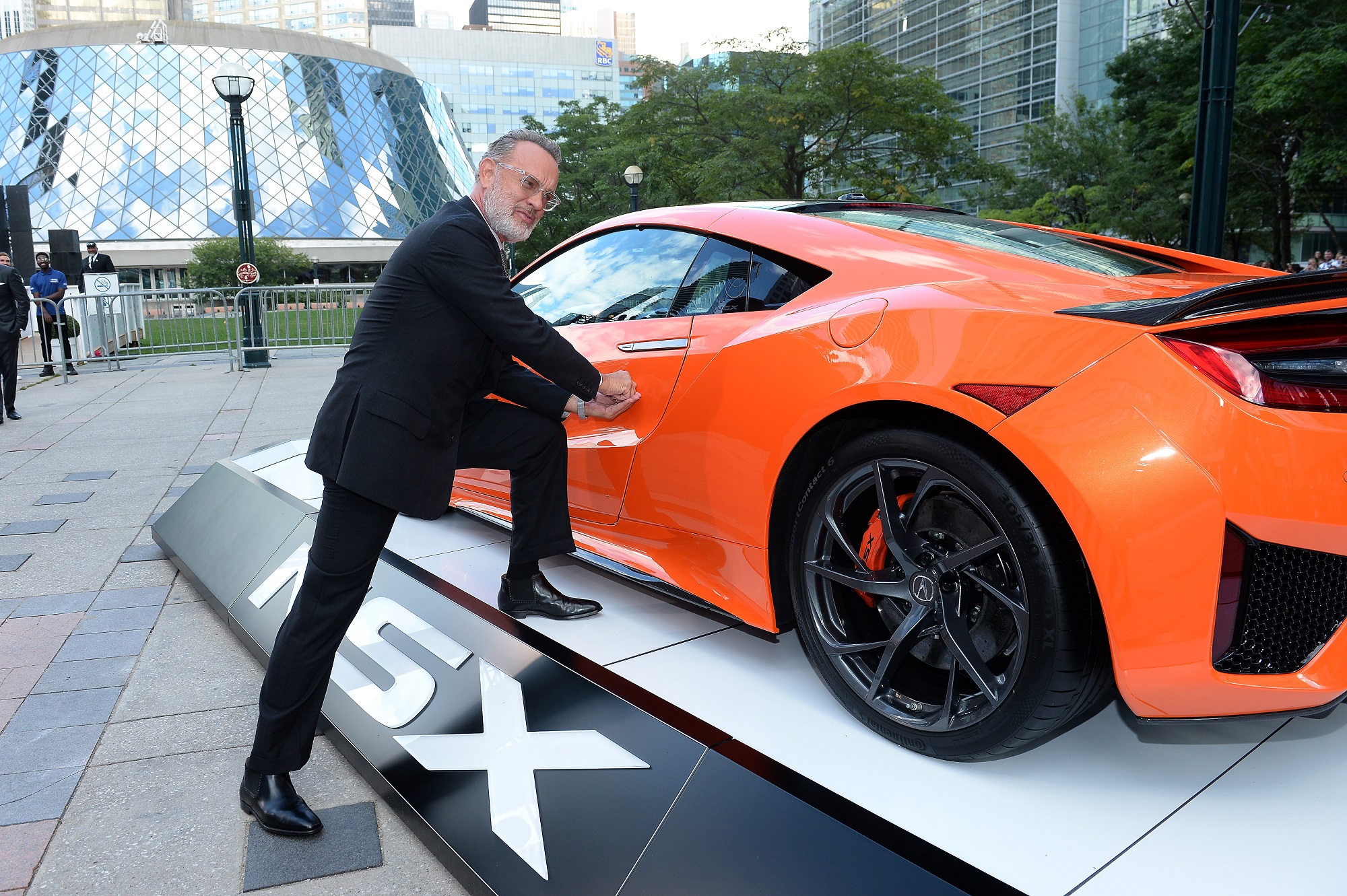 Tom Hanks leaning on an orange car