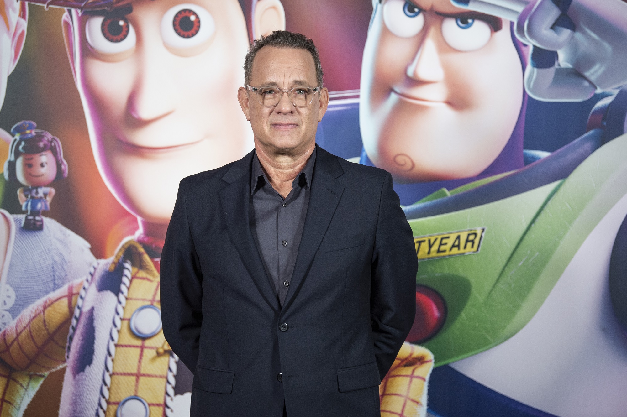 Tom Hanks stands in front of a Toy Story picture