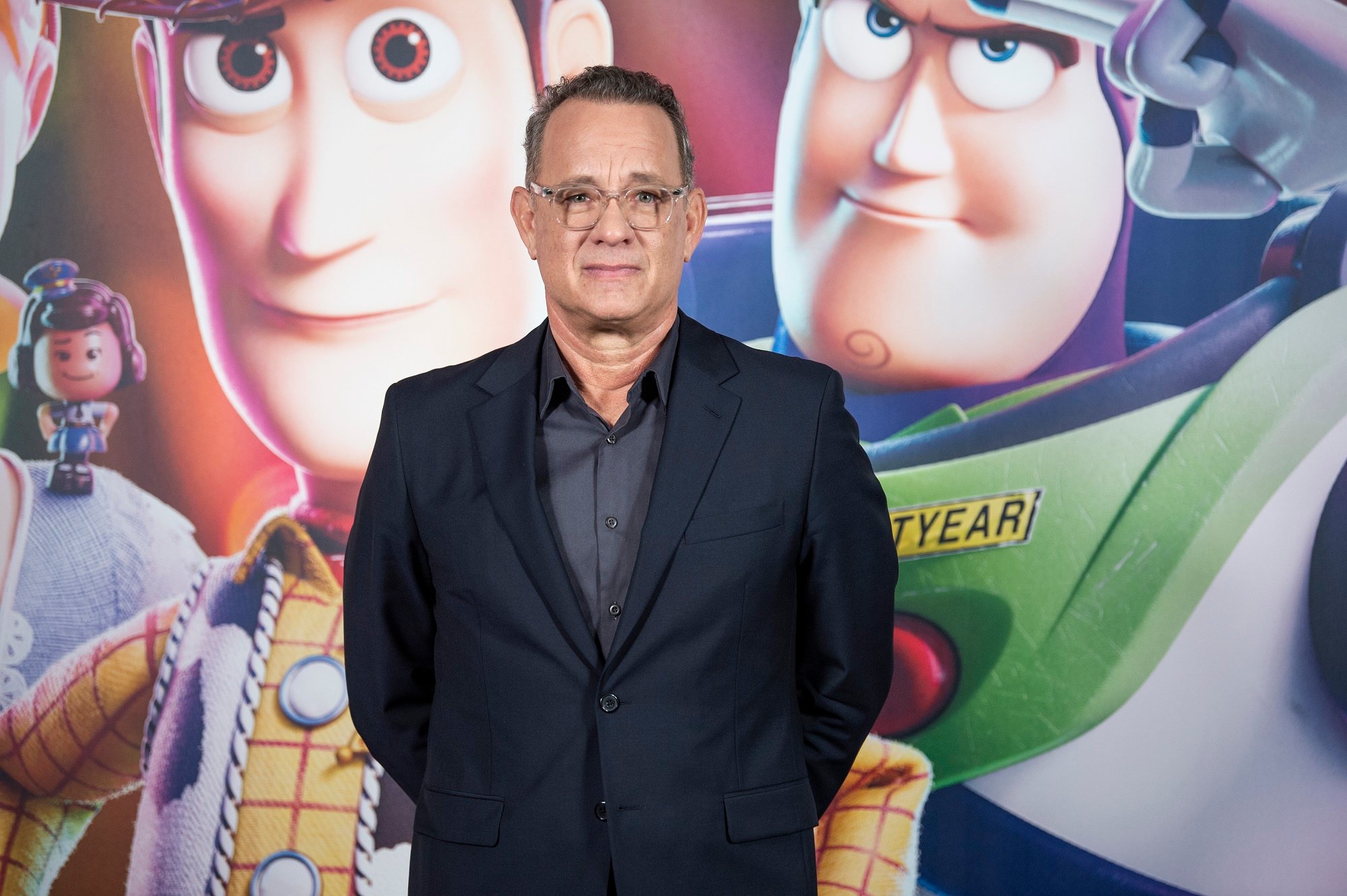 Tom Hanks stands in front of a Toy Story picture