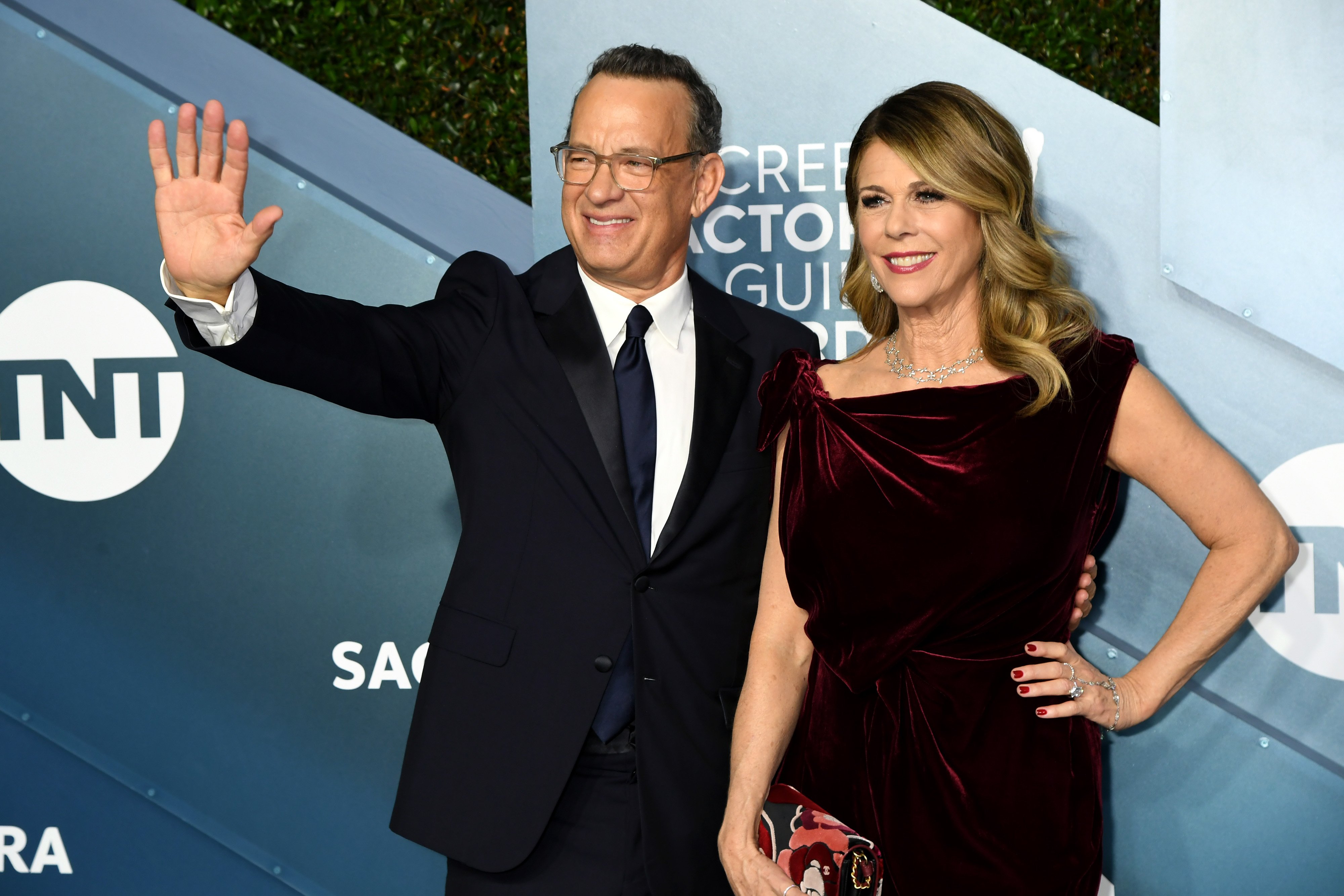 Tom Hanks waves with his other arm around Rita Wilson