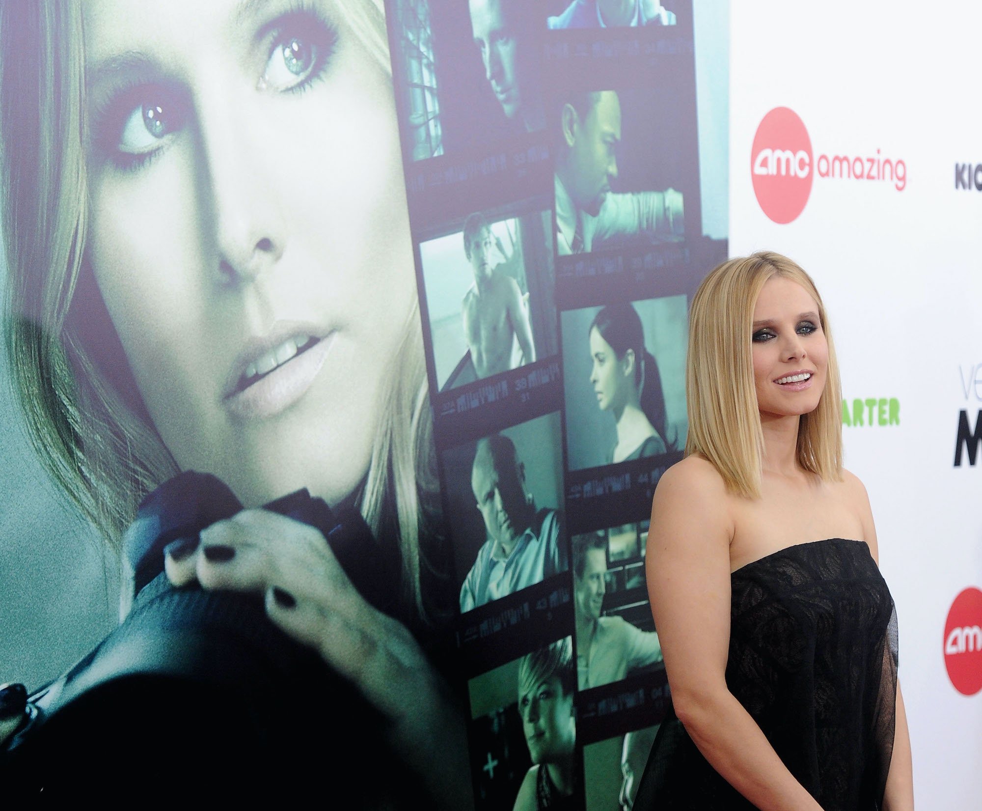 Kristen Bell smiling in front of a 'Veronica Mars' movie posted