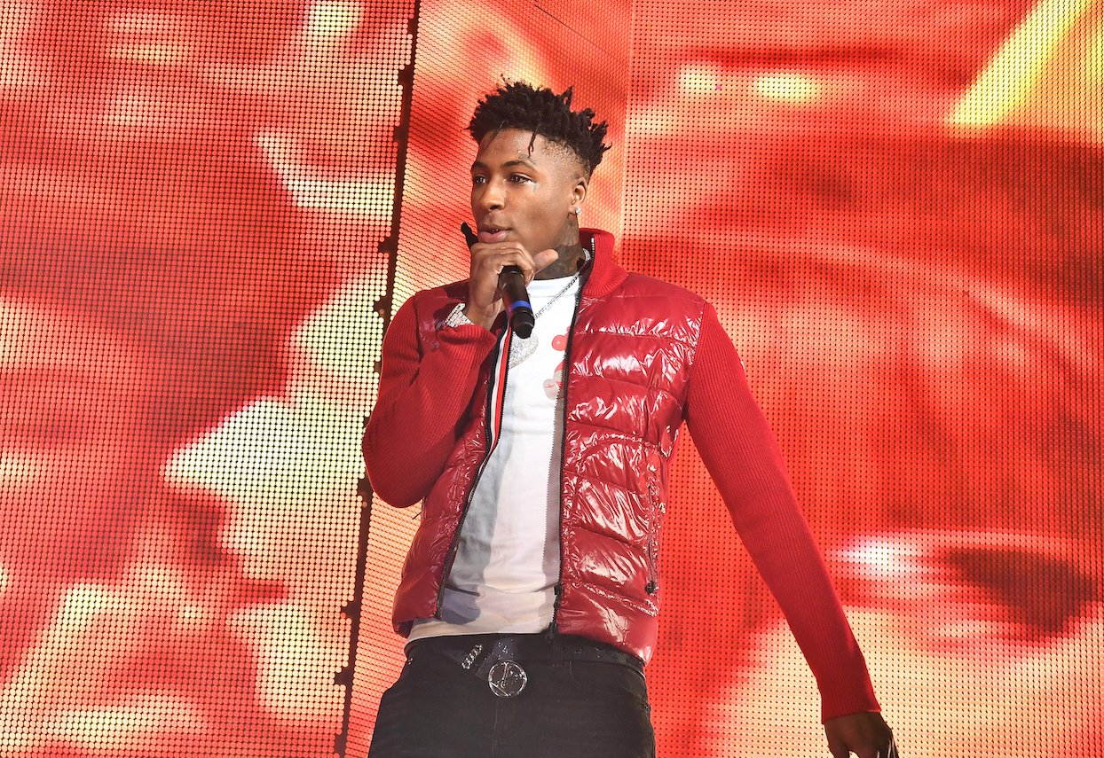 Rapper NBA YoungBoy performing onstage in a red jacket with a microphone in his hand