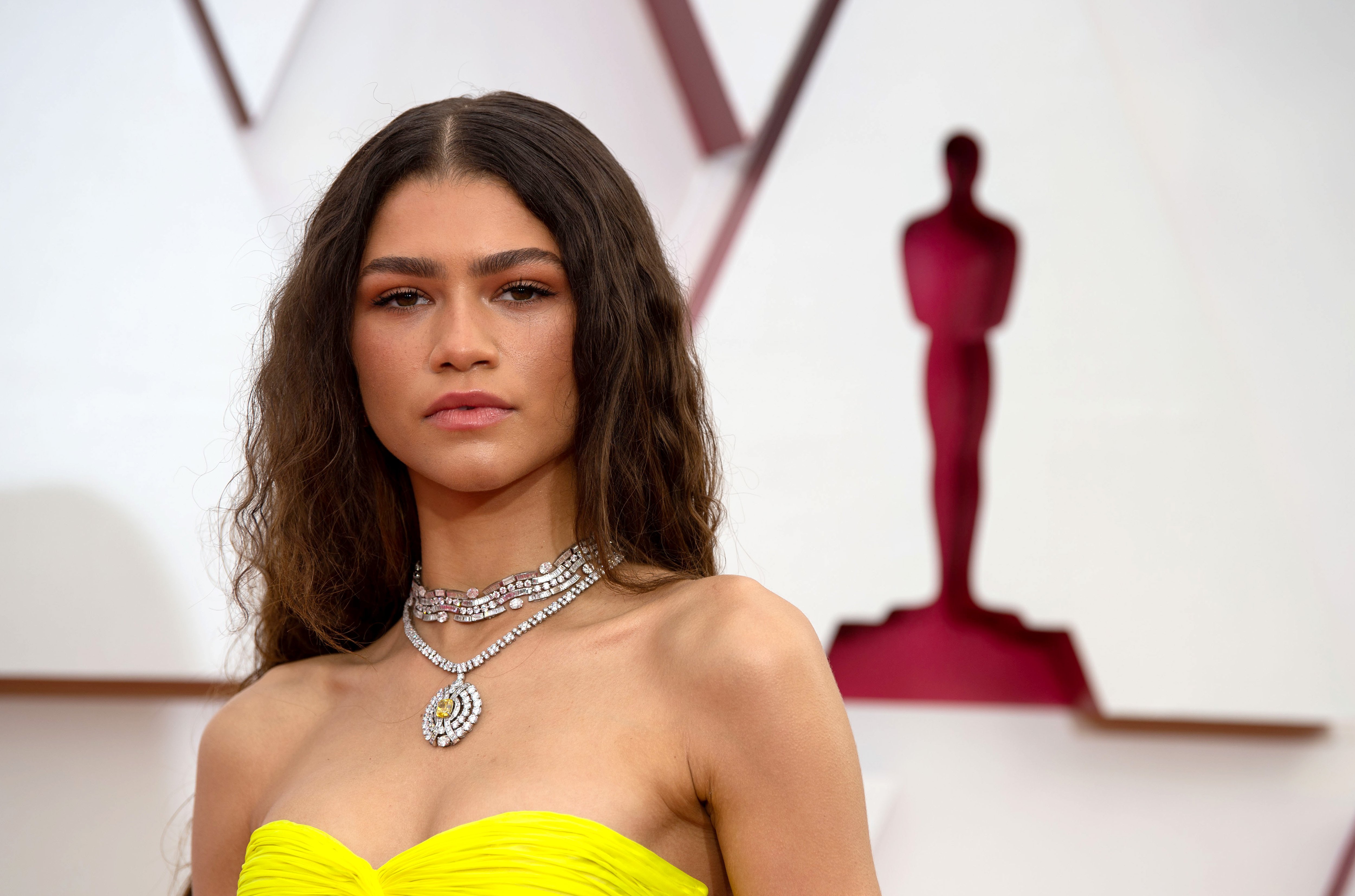 A photo of Zendaya wearing a yellow Valentino gown and a diamond necklace at the Oscars 2021.