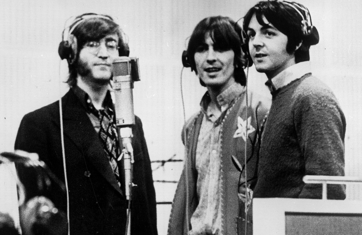 Beatles Lennon, Harrison, and McCartney stand together at a microphone in 1968