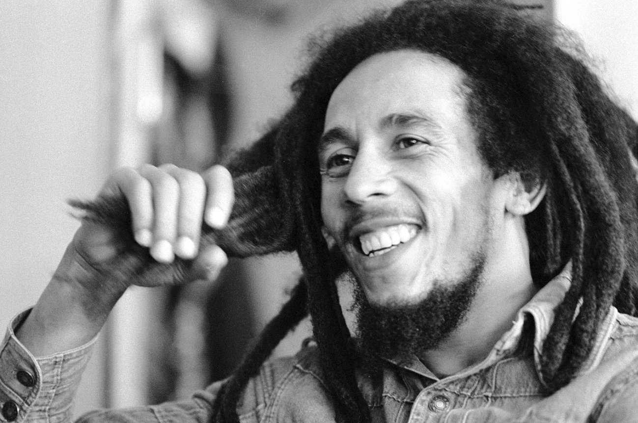 Bob Marley holding a few dreadlocks in his hand and smiling