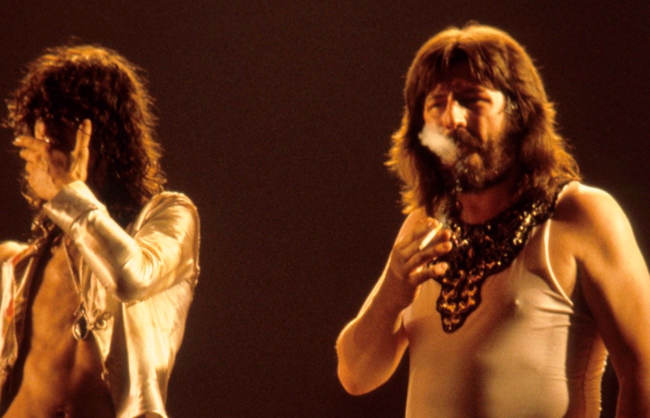 John Bonham blows smoke from a cigarette looking into the crowd as Jimmy Page covers his mouth on stage.