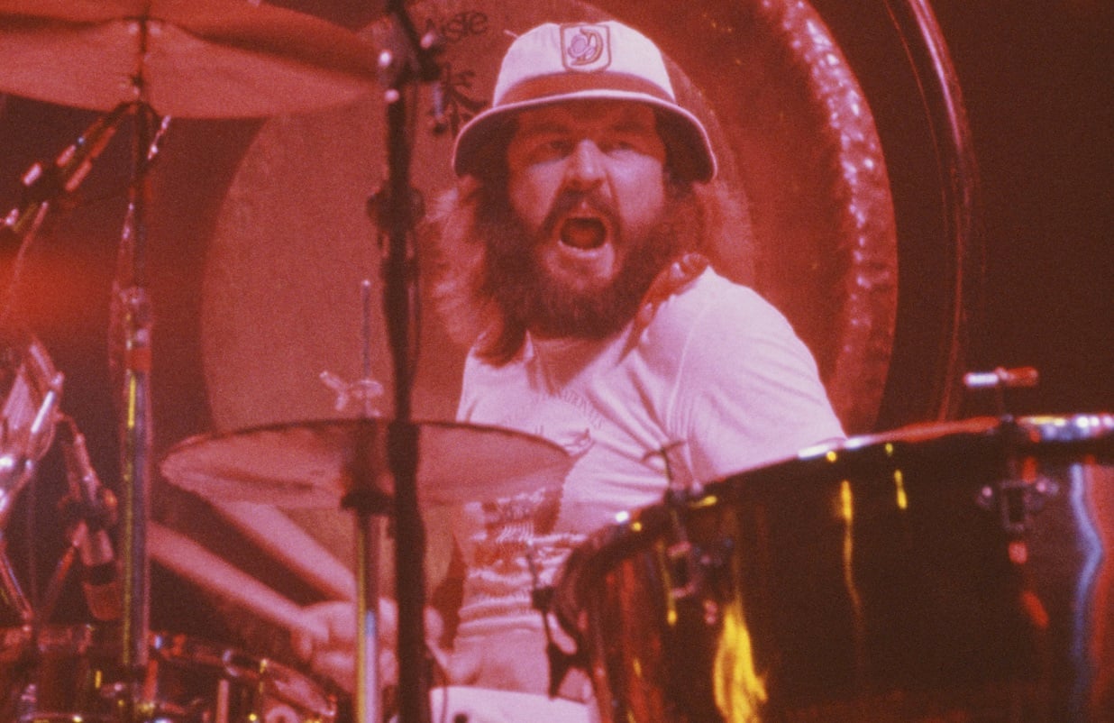 John Bonham, wearing a hat at the drum kit, yells at something off-camera
