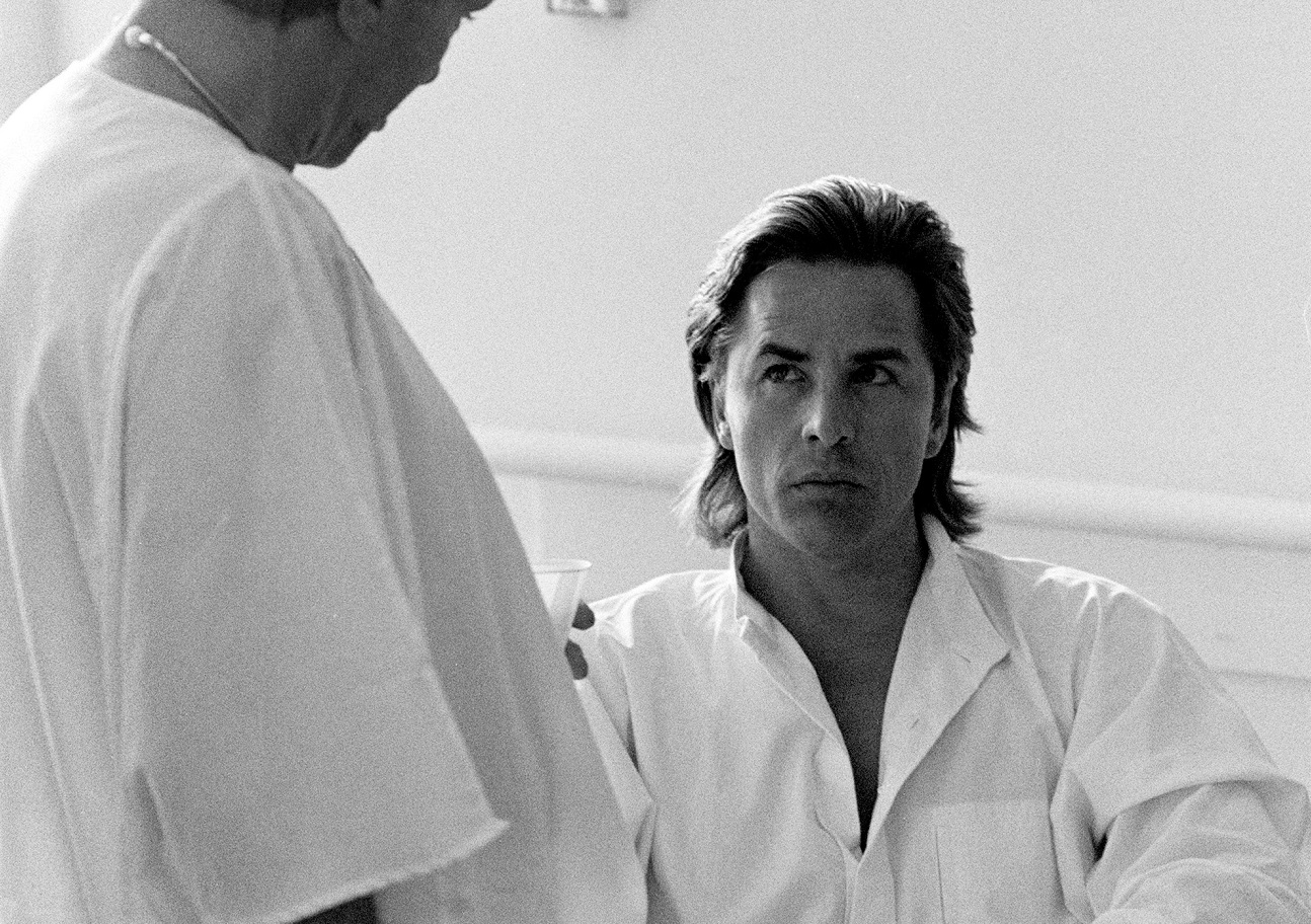 Don Johnson, seated in wheelchair, looks up a doctor in a hospital room