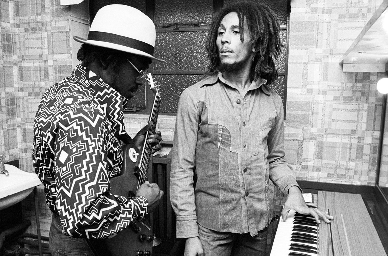 Family Man Barrett plays guitar as Bob Marley stands with his hand on a keyboard