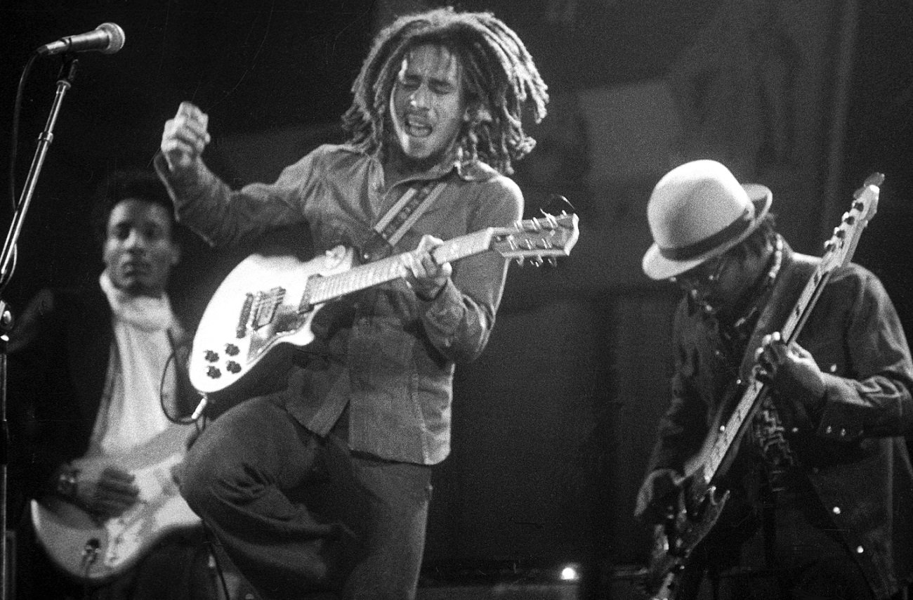 Bob Marley plays guitar with 2 bandmates behind him in 1975