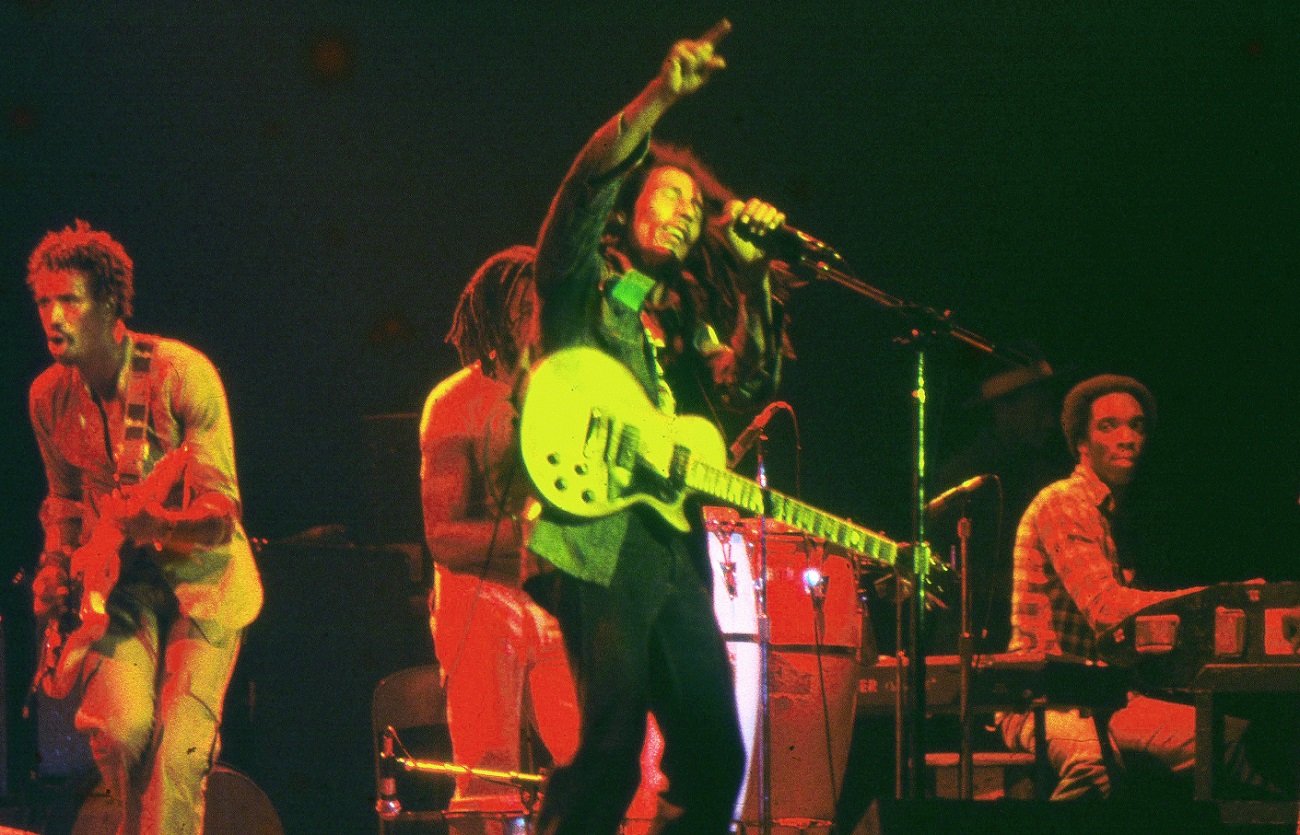Bob Marley performs with eyes closed, holding a microphone and pointing to the sky