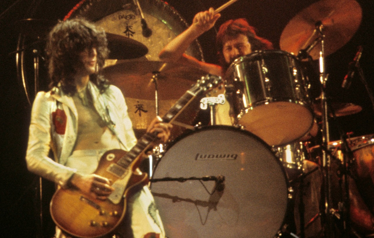 Jimmy Page plays guitar while John Bonham swings his drum stick at his drum kit during a 1977 Led Zeppelin performance