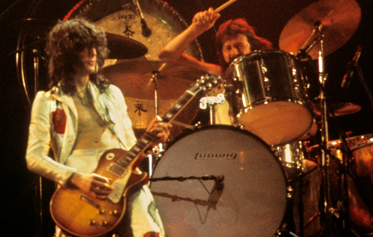 Jimmy Page plays guitar while John Bonham swings his drum stick at his drum kit during a 1977 Led Zeppelin performance