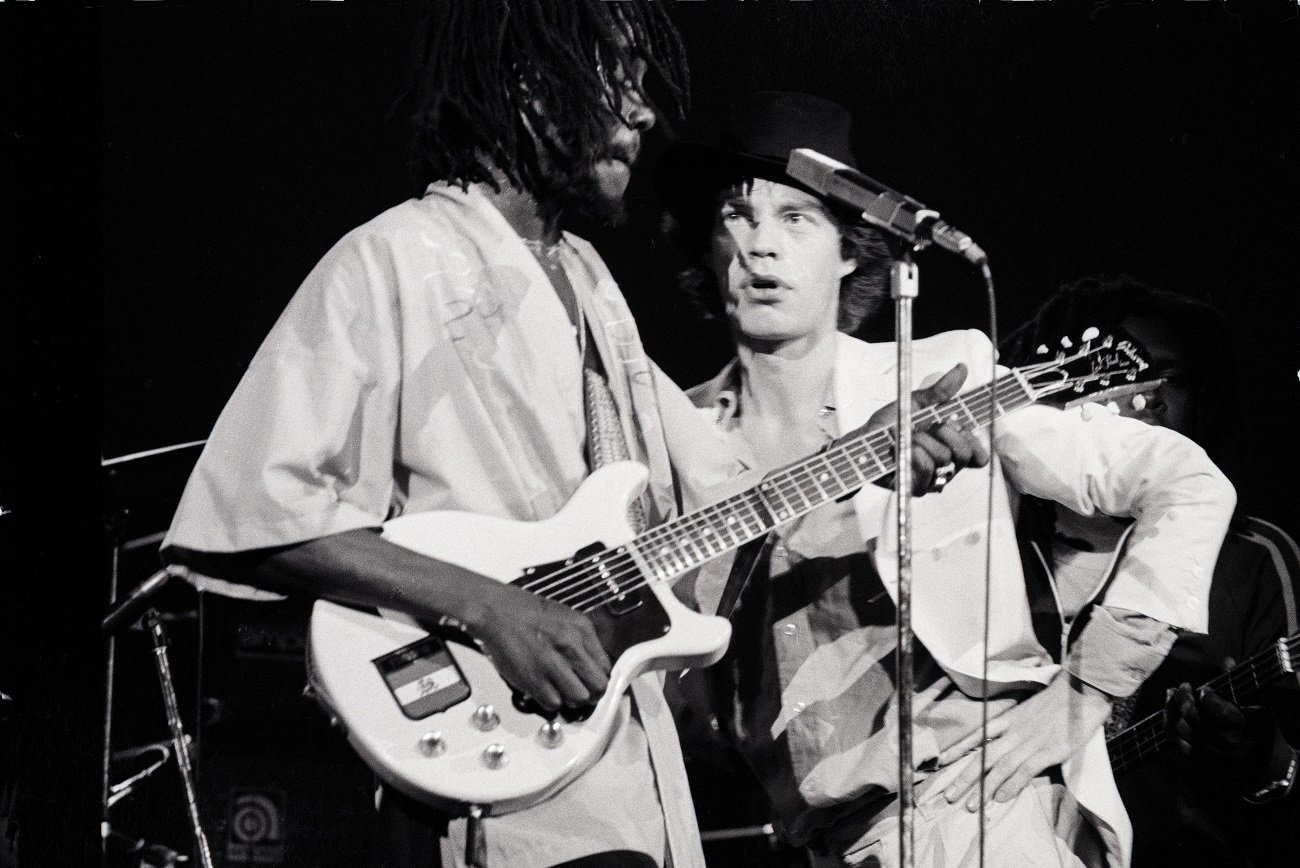 Mick Jagger stands a few feet away looking at Peter Tosh, who plays guitar on stage