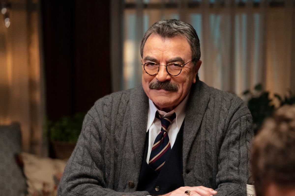 Tom Selleck as Frank Reagan sits at the dinner table in a sweater and tie in 'Blue Bloods' Season 11