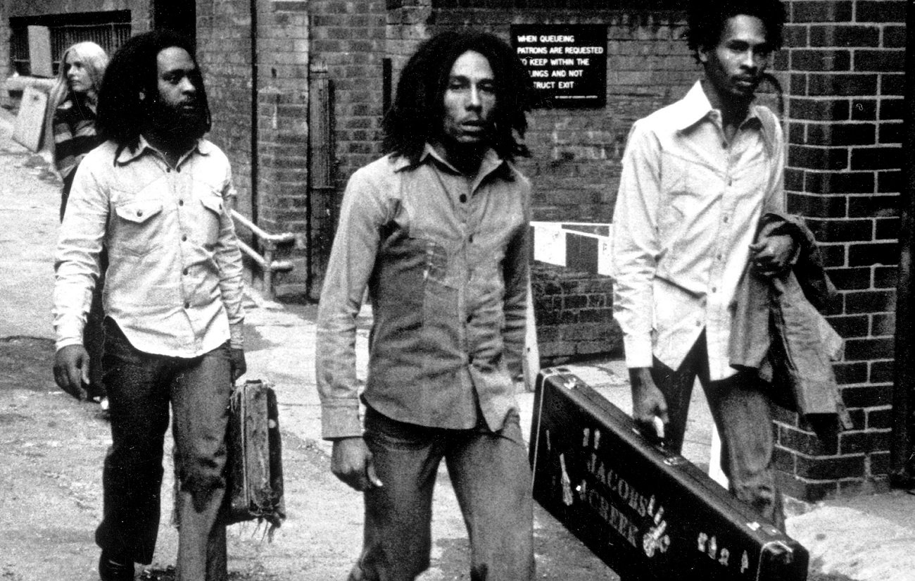 Bob Marley, with two bandmates on either side, looks into the camera en route into a British club