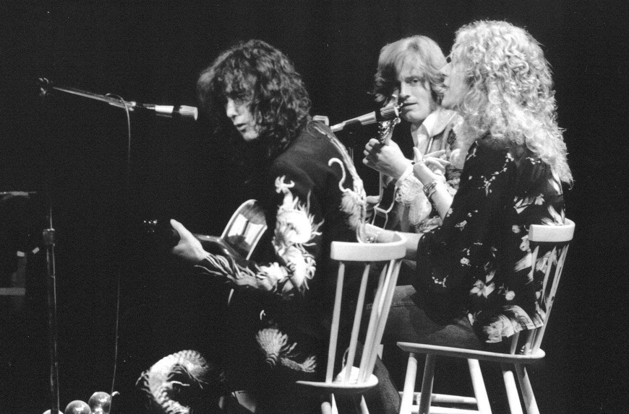 3 members of Led Zeppelin perform on stage while seated