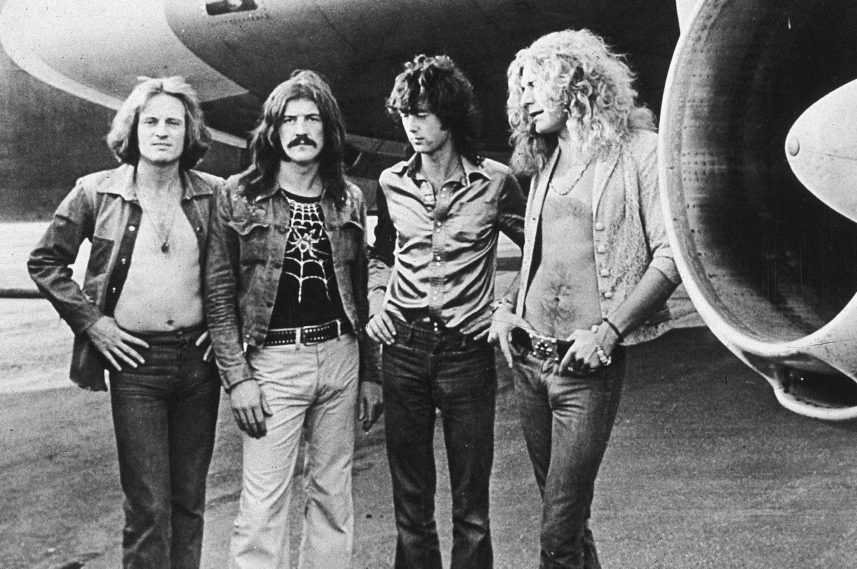 Led Zeppelin posing in front of the wing of the band's airplane in 1973