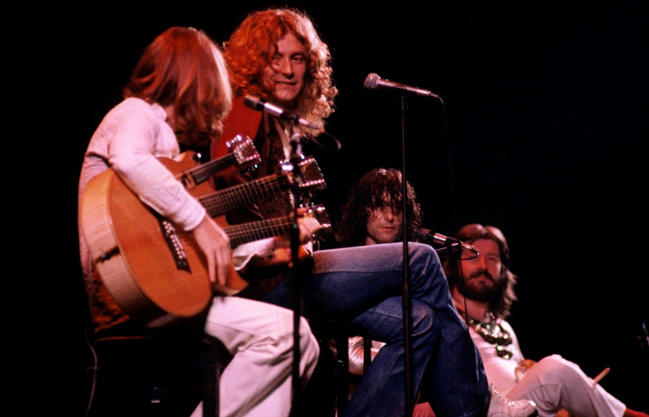 3 members of Led Zeppelin looking at John Paul Jones, who sits with a triple-neck guitar